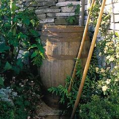 a wooden barrel sitting in front of a stone wall with plants growing on it and a shovel leaning against the top