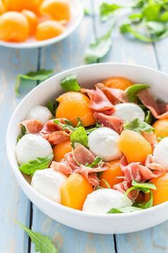 a white bowl filled with oranges and mozzarella on top of a blue table