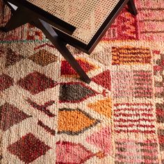 a coffee table on top of a multicolored rug with a wooden frame and metal legs