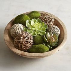 a wooden bowl filled with lots of green succulents on top of a table