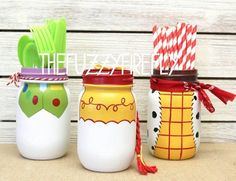 three painted mason jars with spoons and forks in them, sitting on a table