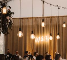 a group of people sitting at tables with lights hanging from the ceiling