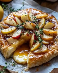 a pastry with apples and herbs on it sitting on a piece of paper next to some lemons