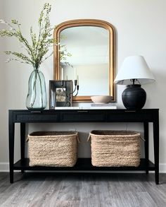 a black console table with two baskets and a large mirror on the wall behind it