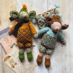 two knitted stuffed animals laying next to each other on a wooden surface with an old book