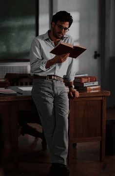 a man sitting at a desk with a book in his hand and looking down on the floor