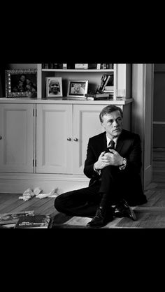 a man in a suit sitting on the floor next to a bookcase and cabinet