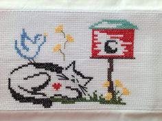 a cross stitch pattern with a cat laying on the ground next to a mailbox