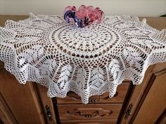 two pink flowers on top of a white doily in a cabinet with wooden drawers