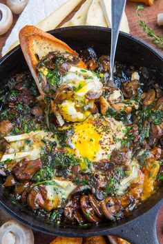 a skillet filled with mushrooms, cheese and an egg in it next to bread