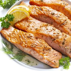 two pieces of salmon on a plate with lemon and parsley