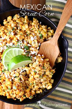 mexican street corn in a cast iron skillet with a wooden spoon and lime wedge