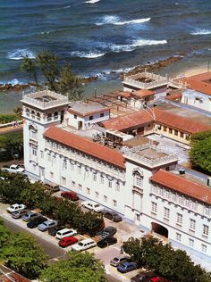 an aerial view of a large white building next to the ocean with cars parked in front of it