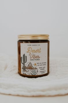 a jar of desert vibes sits on top of a white blanket next to a cactus