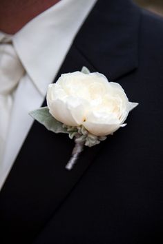 a man wearing a suit and tie holding a white rose in his lapel flower