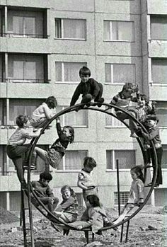 black and white photograph of children playing on playground equipment in front of apartment building with windows