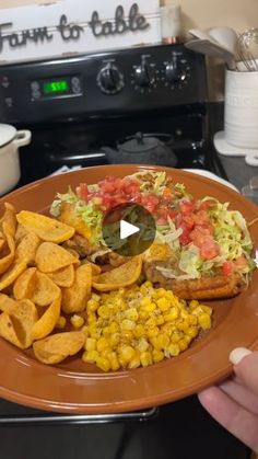 a plate with chips, coleslaw and corn on it is being held in front of an oven