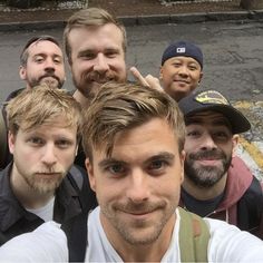 a group of men standing next to each other in front of a parking lot with one man taking a selfie