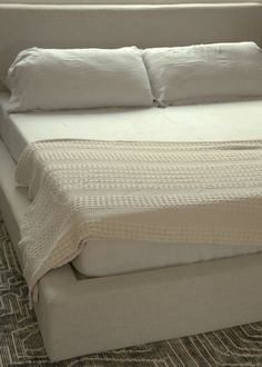 a bed with white sheets and pillows on top of it in a room that has carpeted flooring