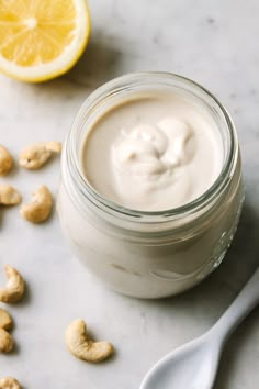 a glass jar filled with yogurt next to a lemon and cashews