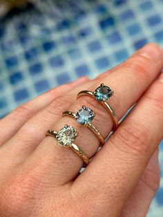 three different rings on someone's hand, one with an aqua topazte