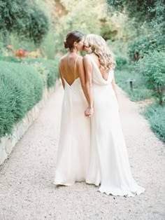 two women in white dresses walking down a path