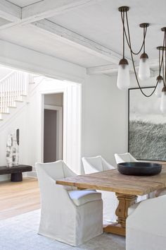 a dining room table with white chairs and a bowl on top of it in front of a staircase