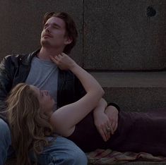 a man and woman laying on the ground next to each other with their arms around one another