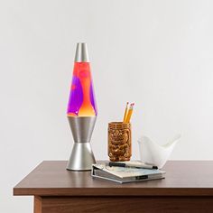 a wooden table topped with a blue and green vase next to a cup filled with pencils