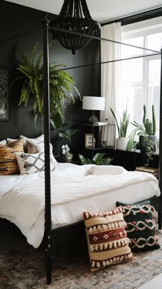 a bedroom with black walls and white bedding, potted plants on the side