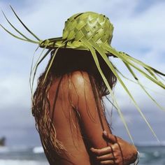 a woman wearing a straw hat on top of her head at the ocean's edge