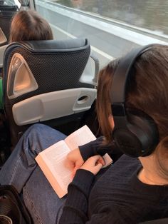 two people are sitting on a bus with headphones and books in their hands as they look out the window