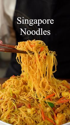 someone holding chopsticks over noodles in a white bowl with the words singapore noodles on it