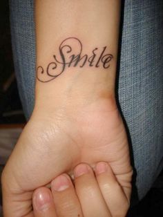 a small wrist tattoo with the word smile on it