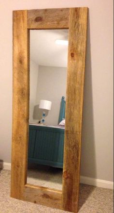 a large wooden mirror sitting on top of a floor next to a lamp and dresser