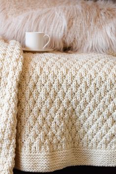 a coffee cup is sitting on top of a blanket that has been made into a crocheted afghan