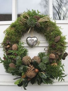 a wreath with pine cones, evergreens and other greenery on the front door