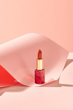 a red lipstick is laying on a pink surface and it's shadow has been cast