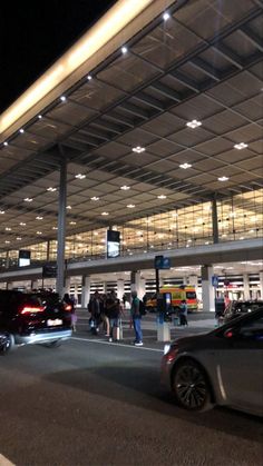 cars parked in front of an airport terminal at night with people standing outside the building