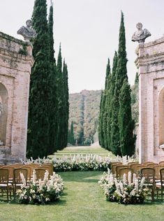 an outdoor ceremony set up with chairs, flowers and greenery in front of stone archways