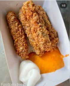 two fried chicken sticks with sauce in a paper container