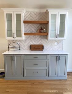 a kitchen with gray cabinets and white marble counter tops, wood flooring and wooden shelves