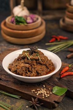 a white bowl filled with meat on top of a wooden cutting board next to spices and herbs