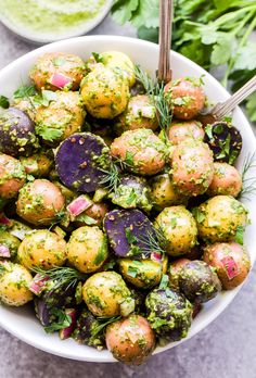 a white bowl filled with potatoes covered in herbs and seasoning next to other vegetables