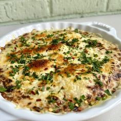 a casserole dish with cheese and herbs in it sitting on a white plate