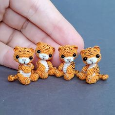 three small crocheted animals sitting next to each other on a gray surface in front of a person's hand