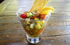 a small glass filled with salad and chips on top of a wooden table