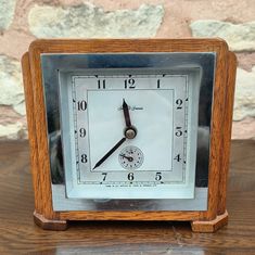 an old wooden clock sitting on top of a table next to a brick wall in the background