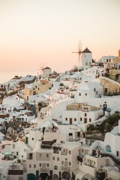 white buildings with windmills on the top of them at sunset in oia, greece