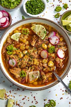 a bowl filled with meat and vegetables on top of a white table next to limes